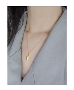 Close-up of a minimalist gold opal pendant necklace worn by a model in a gray suit