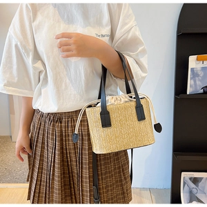 Detail of straw bucket bag featuring black PU straps and beige drawstring inner pouch