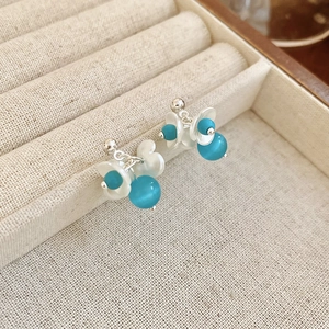 Close-up of pearl flower earrings with blue cat-eye stone on beige linen display