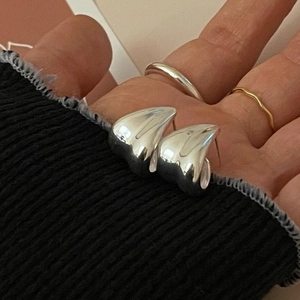 Macro shot of silver heart-shaped stud earrings showing scale on model's fingers