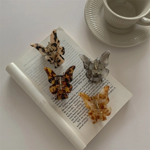 Set of four butterfly-shaped tortoiseshell hair claws in assorted colors on an open book