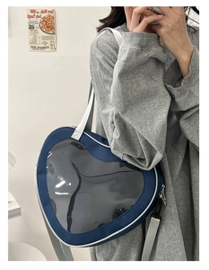 Blue heart-shaped ita bag with clear window and white canvas strap shown in use