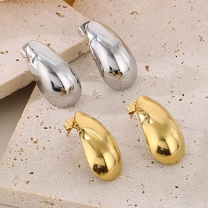 Macro shot of polished gold and silver teardrop earrings on a textured stone base