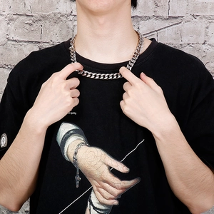 Close-up of a silver stainless steel cuban link chain worn by a male model on a wall background