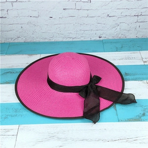 Detail of deep pink woven straw hat with wide brim and elegant black ribbon bow