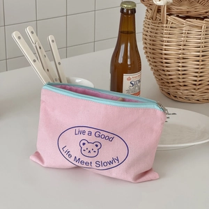 Detailed view of a pink canvas pouch with blue zipper and cute bear print in a cozy setting