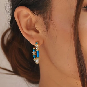 Macro view of C-shaped boho earring with white pearls and turquoise beads on ear
