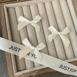 Detailed view of three cream white satin ribbon bow clips on soft linen jewelry padding