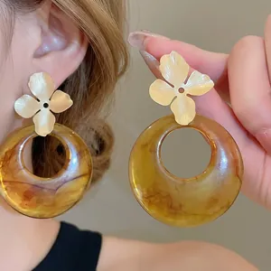 Golden flower studs with large amber resin hoop earrings for a stylish statement look