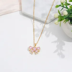 Elegant gold bow necklace with pink zircon stones on a white and marble background