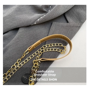 Detail of golden metal chain strap with brown leather shoulder pad on a grey fabric
