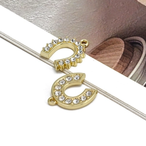 Macro detail of gold U-shaped horseshoe pendant with clear rhinestones for DIY jewelry
