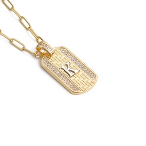 Détail du pendentif rectangulaire doré avec lettre K sertie sur une chaîne trombone