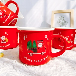 Detail of red Christmas ceramic mugs with Santa Claus and tree patterns on lace cloth