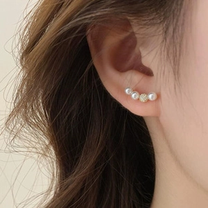 Detailed close-up of curved gold stud earrings with white pearls and pavé crystal ball