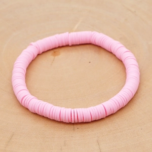 Detail van roze Heishi-kralenarmband op natuurlijk houtoppervlak in boho-stijl