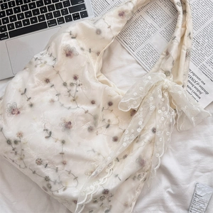 Detail of cream shoulder bag with floral embroidery and white lace bow decoration