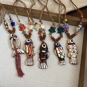 Detailed flat lay of handcrafted ceramic fish pendants with ethnic braided cords and beads