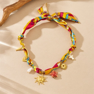 Detail of silk scarf necklace with gold sun, heart and starfish pendants on beach sand