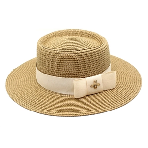 Classic straw boater hat with beige ribbon and vintage bee metal charm on white background