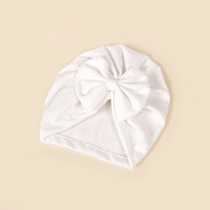 Close-up of white waffle knit texture and large handmade bow on baby turban hat