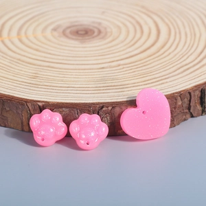 Macro shot of glittery pink cat paw and heart-shaped resin beads on a wood slice