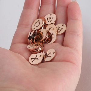 Gros plan de pendentifs ronds en acier inoxydable or rose avec lettres pour bijoux DIY