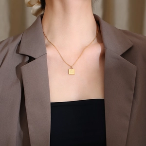 Detail of model wearing a gold square rose pendant necklace with a brown blazer