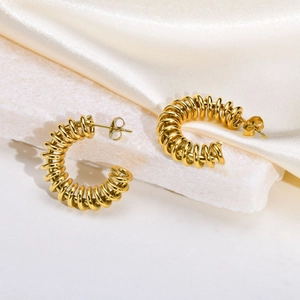 Detail of gold twisted spiral C-hoop earrings on white stone and silk background