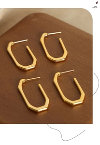 Detail view of four gold geometric hexagonal hoop earrings on dark walnut wood display