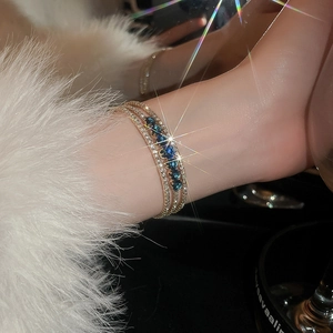Detailed close-up of triple-layered gold bracelet with blue marquise zircon stones