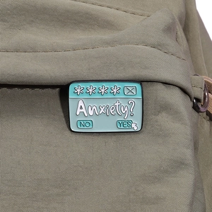Close-up of a blue enamel anxiety prompt badge pinned on a green canvas backpack