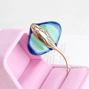 Macro shot of golden manta ray brooch with blue gradient enamel in velvet box