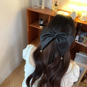 Close-up of a large black satin bow hair clip with elegant white pearl pendants
