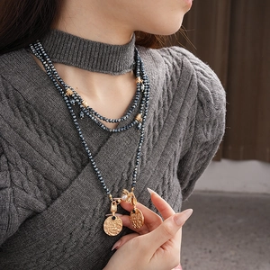 Detail of vintage gold embossed charms and layered grey beads on a grey sweater