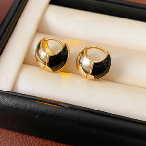 Close-up of golden round hoop earrings with black enamel on a beige velvet jewelry box