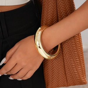 Close-up of a polished gold tubular bangle worn with a stylish brown woven handbag