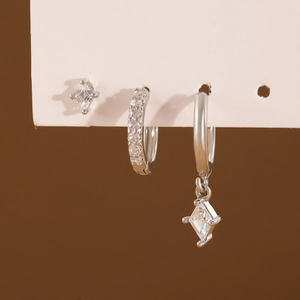 Set of three silver rhombus zircon earrings with hoop and stud styles on display