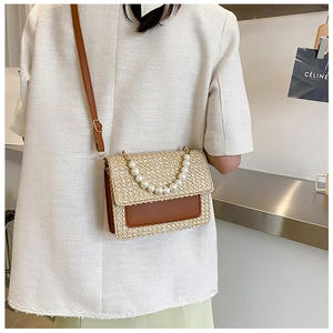 Detail of straw and brown leather shoulder bag with pearl accents worn by a model
