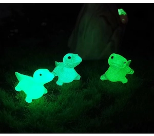 Close-up of three luminous resin turtle figurines glowing green on moss in the dark
