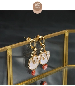 Detailed shot of gold baroque pearl earrings with butterfly and red heart charms on glass