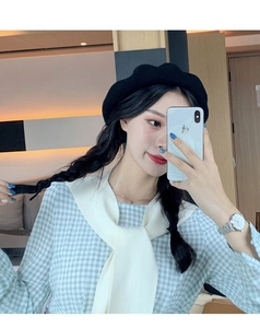 Close-up of a classic black wool beret worn with a white knit shawl and blue checkered shirt
