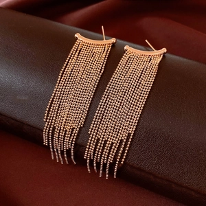 Close-up of rose gold tassel earrings displayed on a dark brown leather jewelry case