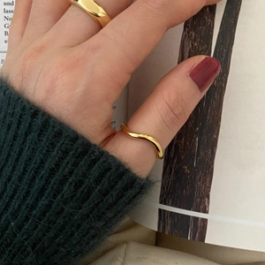 Minimalist wavy 925 silver ring in gold finish worn on hand over a book background