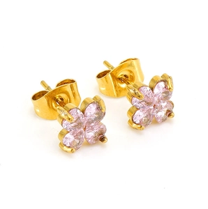 Gros plan de boucles d'oreilles trèfle dorées avec zircon rose sur fond blanc pur
