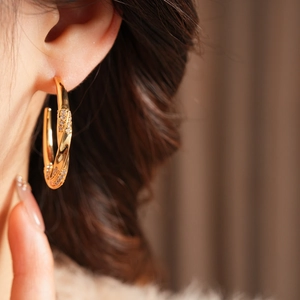 Close-up of model wearing gold-plated C-shaped twist earrings with shimmering zircons