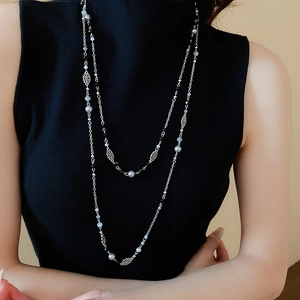 Detail of silver layered necklace with flower pendants and pearls on a black sweater