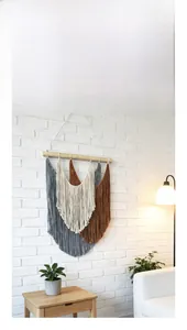 Detail of woven boho wall tapestry with grey, beige and brown long tassels on wood pole