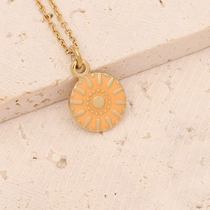 Macro detail of a golden cross chain necklace with orange enamel sunburst charm on stone