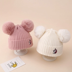 Detail of ribbed knit winter hats with unicorn embroidery and double faux fur pom-poms